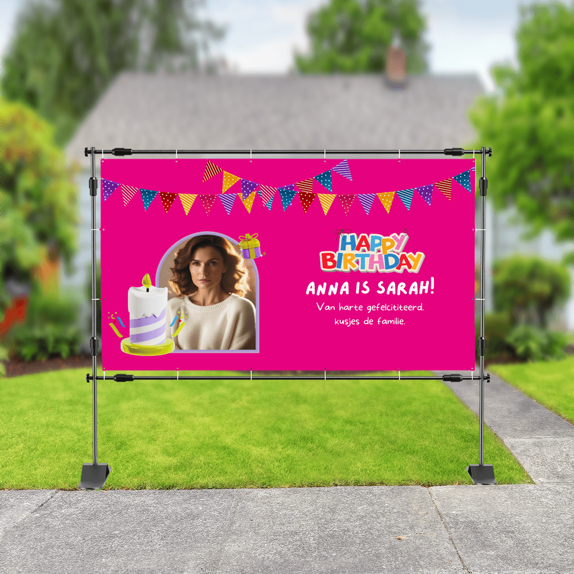 Verjaardagsspandoek met roze achtergrond, slingers, foto van vrouw, illustraties van taart en cadeau en tekst 'Anna is Sarah! Van harte gefeliciteerd. Kusjes de familie.' met kleurrijk 'Happy Birthday'-logo