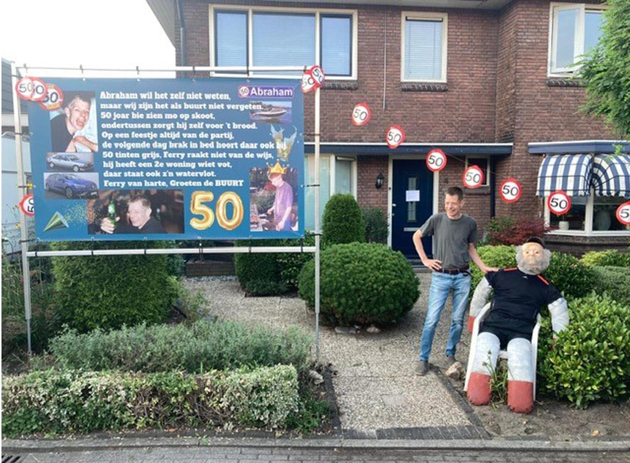 Een Abraham die een spandoek in de tuin heeft hangen, die in een frame gemaakt is. Verder is de tuin versierd met een pop en staat de jarige te poseren.