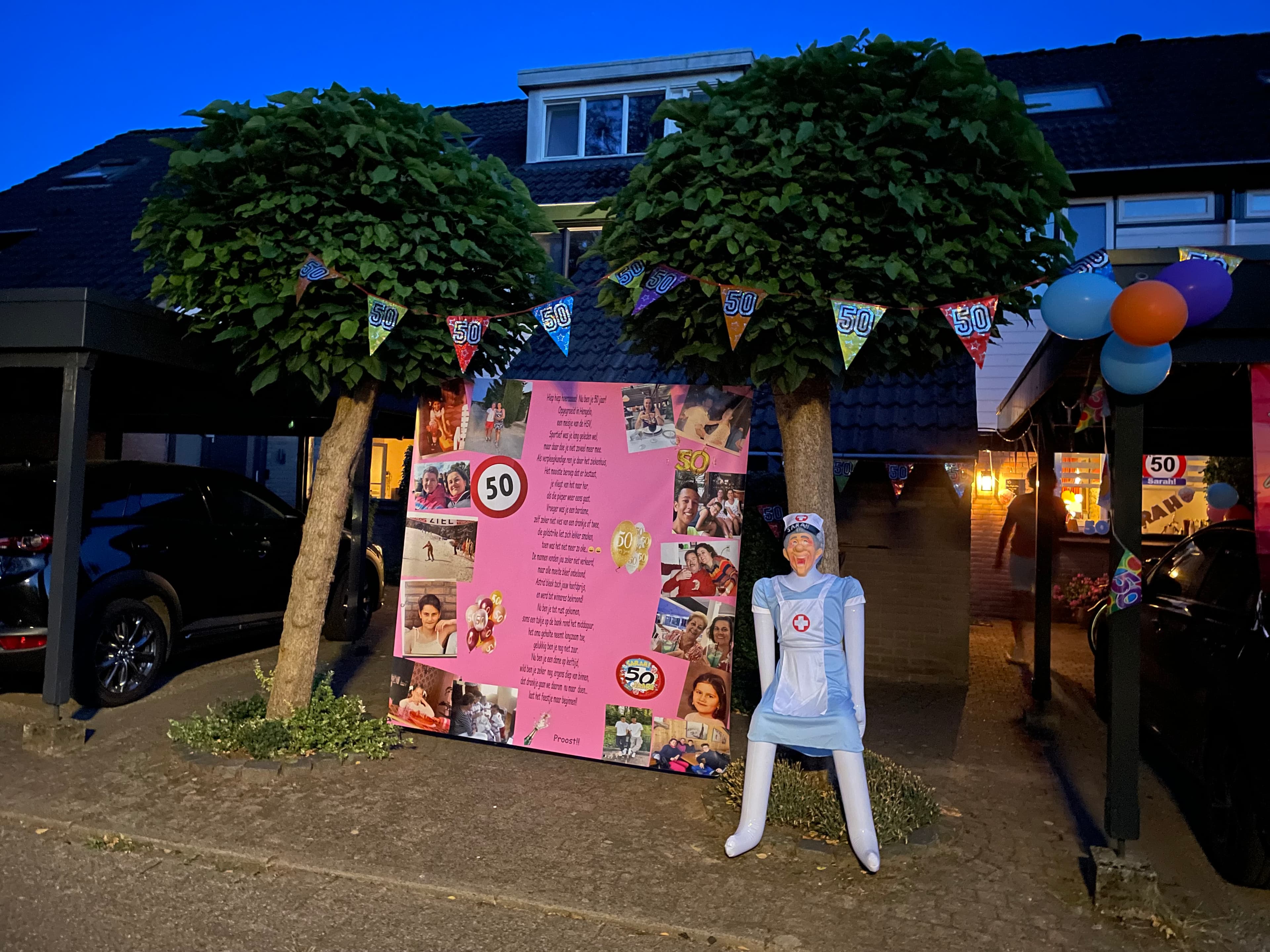 Roze spandoek voor een Sarah. Op dit spandoek staan foto's aan de zijkanten en tekst in het midden. Naast het spandoek is er een pop neergezet.