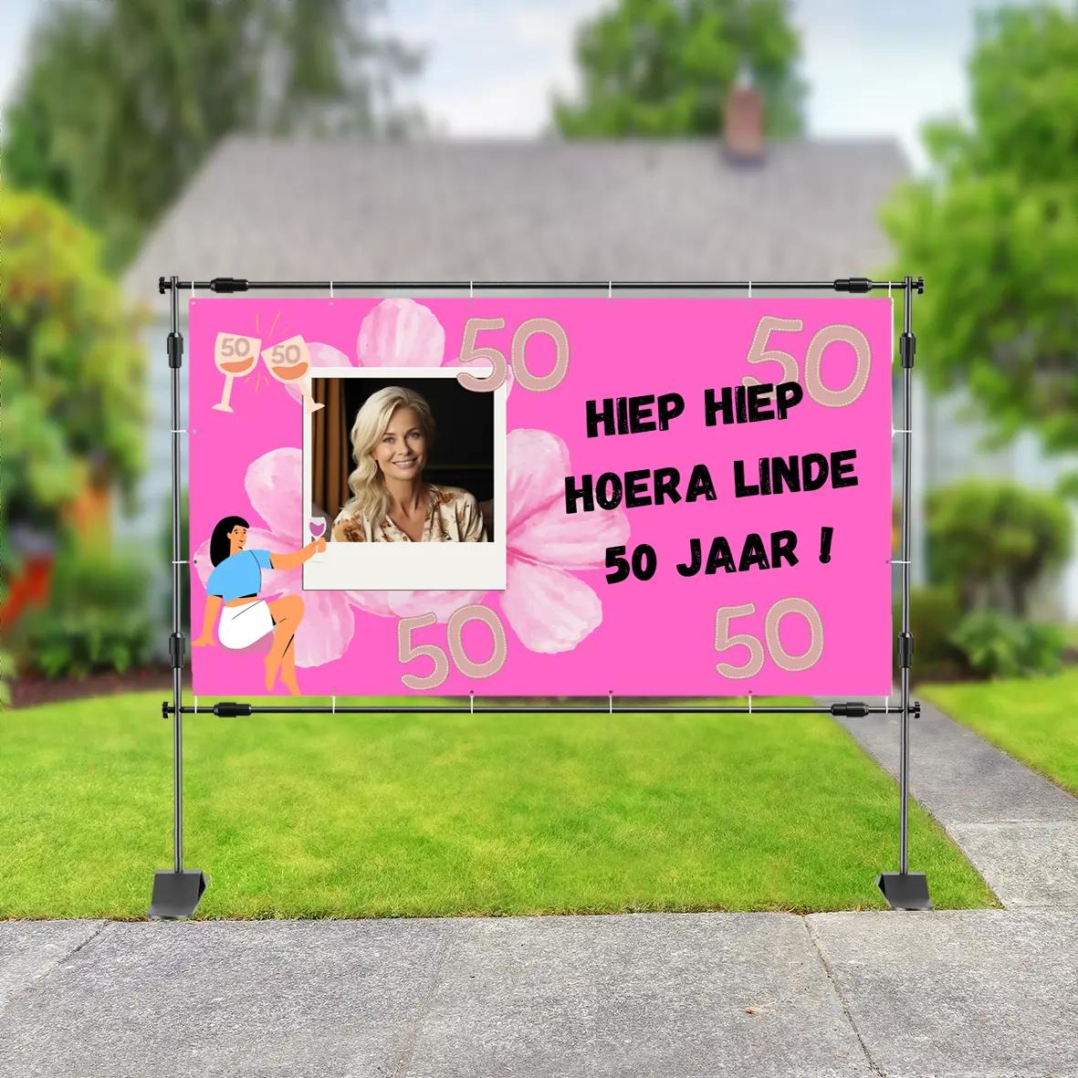 Spandoek teksten – Hiep hiep hoera! Linde viert haar 50e verjaardag met een vrolijk roze spandoek, versierd met bloemen, het getal 50 en een persoonlijke foto.
